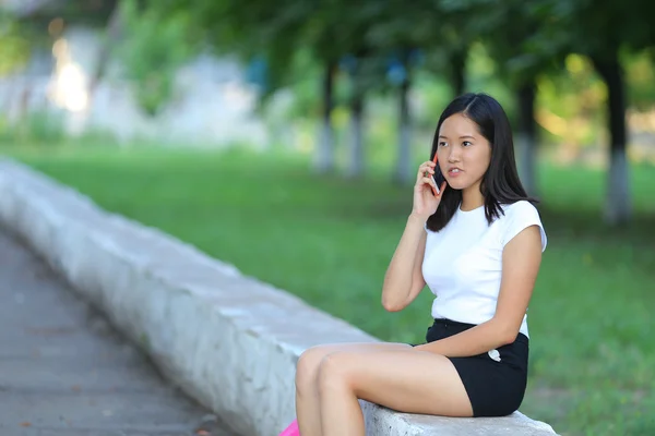 年轻的女孩坐在和谈在公园里电话 — 图库照片