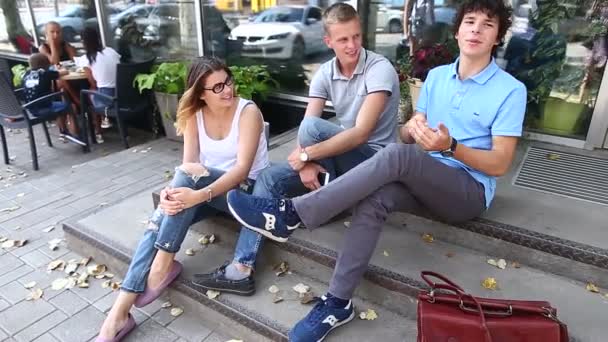 Jóvenes tres amigos sentados piso en la calle, hablando, usando — Vídeo de stock