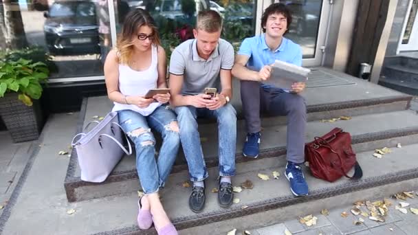 Jovens três amigos sentados no chão na rua, falando, usando — Vídeo de Stock