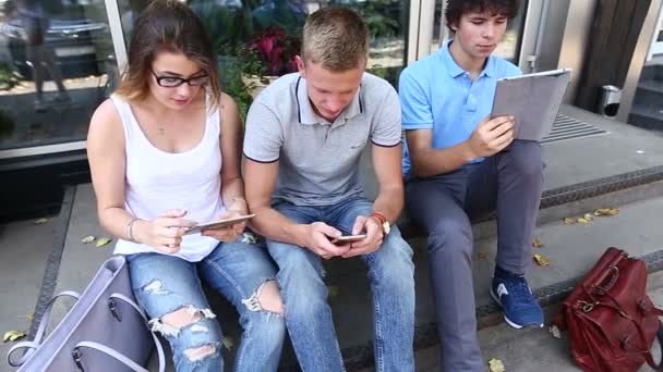 Молодые трое друзей сидят на улице, разговаривают, используют — стоковое видео
