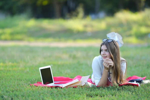 Jeune fille couchée sur l'herbe dans le parc et travaille à un ordinateur portable . — Photo