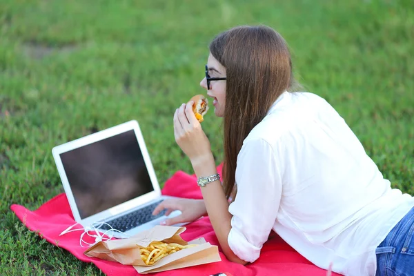 Молодая девушка о природе быстрого питания и работы на ноутбуке — стоковое фото