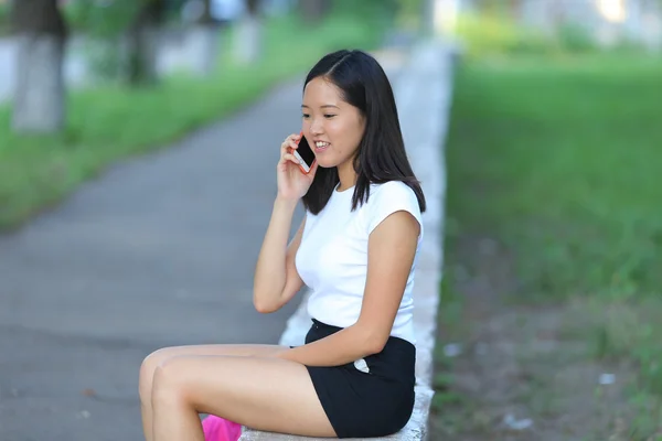 Fiatal lány ült, és beszél a telefonon, a parkban — Stock Fotó