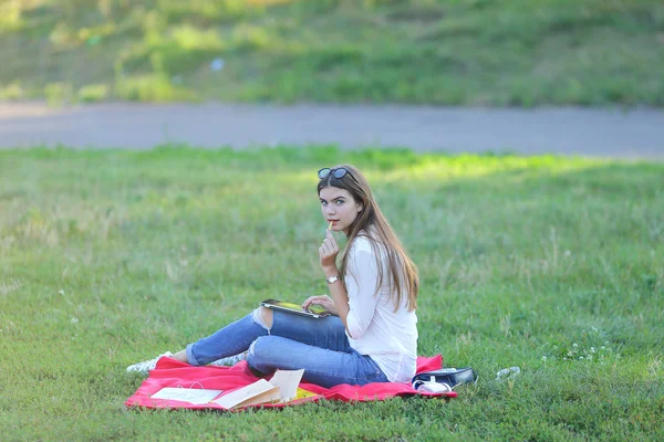 Giovane ragazza seduta sull'erba nel parco lavora in un computer portatile e mangiare fast food — Foto Stock