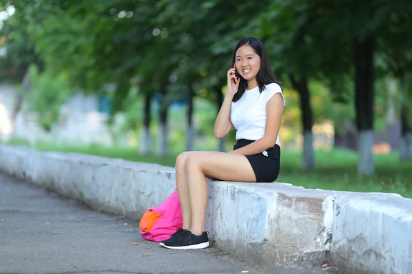 Mladá dívka sedí a mluví po telefonu v parku — Stock fotografie