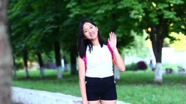 Kvinnan vinkar hand och ler till kamera och berör hår på en gree — Stockvideo