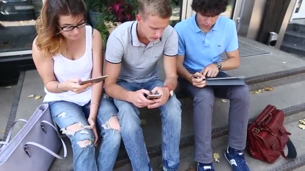 Young three friends sitting floor in the street, talking, using — Stock Video