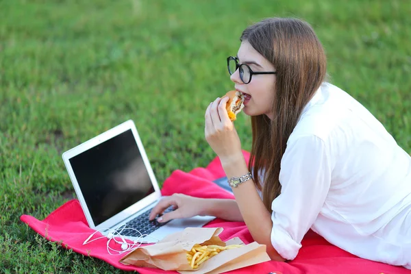 Junges Mädchen über die Natur des Fastfood-Essens und die Arbeit am Laptop — Stockfoto