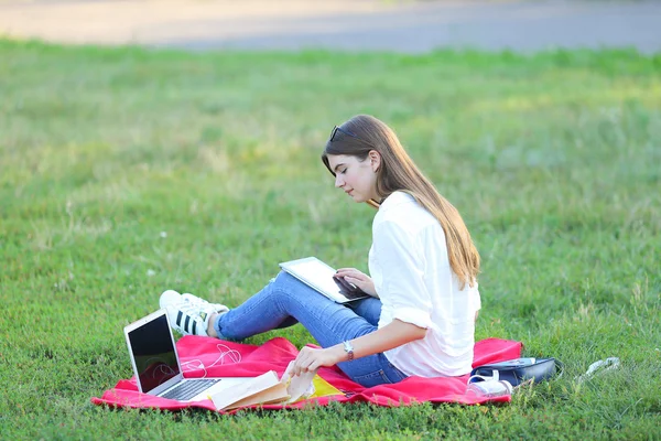 Jeune fille assise sur l'herbe dans le parc travaille à un ordinateur portable et manger de la restauration rapide — Photo