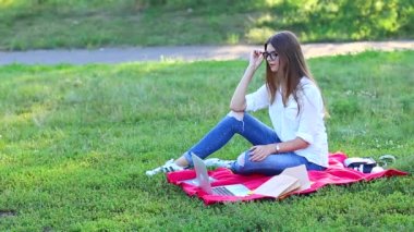 parkta oturan ve kulaklık ile bir dizüstü bilgisayar üzerinden Skype'takonuşurken Bayan