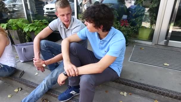 Трое молодых друзей сидят на улице, разговаривают, используют планшет, телефон — стоковое видео