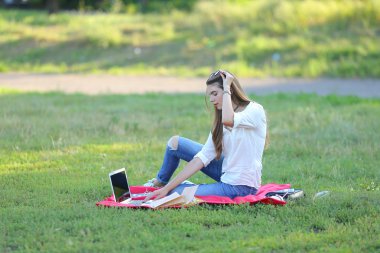 park ve çalışan bir dizüstü bilgisayar, çimlerin üzerine oturan genç kız.