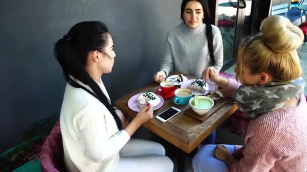 Tre belle donne sorridono nel caffè, parlare, raccontare segreti, mangiare, bere caffè . — Video Stock