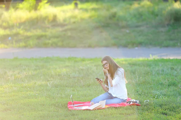 Jeune fille assise dans le parc, souriant et travaillant à son ordinateur portable, écoutant de la musique — Photo