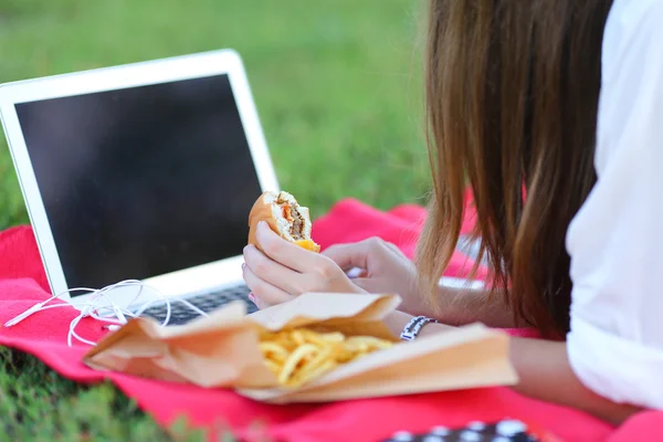 Junges Mädchen über die Natur des Fastfood-Essens und die Arbeit am Laptop — Stockfoto