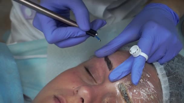 El esteticista de las manos hace el procedimiento El paciente dibuja las cejas Mikrobleyding cliente tatuaje permanente, reconstrucción de la ceja, pigmentación micro — Vídeos de Stock