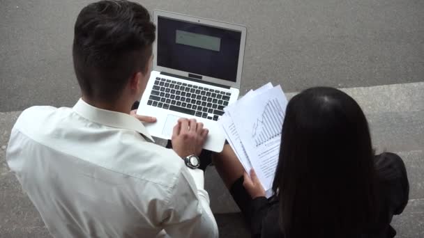 Joven hermosa mujer de negocios femenino y caucásico uso masculino documentos, teclado de prensa portátil sentarse en las escaleras del edificio de oficinas — Vídeo de stock