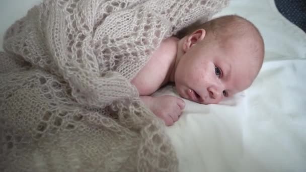 Новорожденный младенец лежит на кровати в трикотажной одежде — стоковое видео