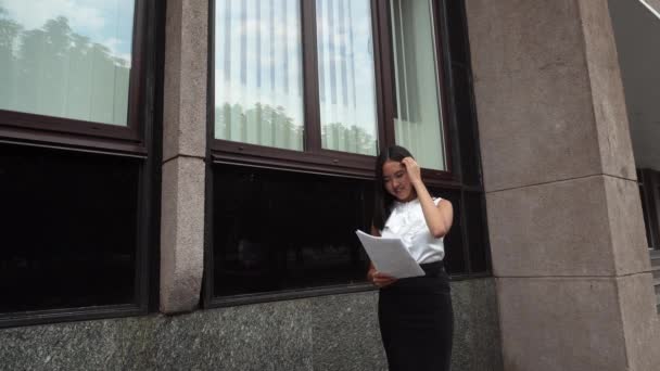 Joven hermosa mujer de negocios mujer mujer retrato mirar documentos soportes en segundo plano edificio de oficinas al aire libre — Vídeos de Stock