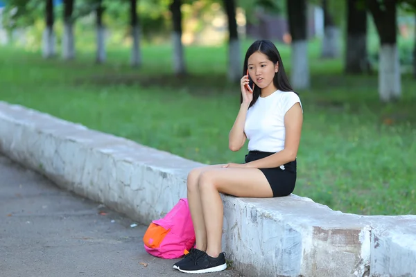 Chica joven sentada y hablando por teléfono en el parque — Foto de Stock