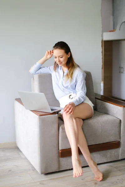 Mujer joven que trabaja con el ordenador portátil en casa y sentado en el sofá. — Foto de Stock