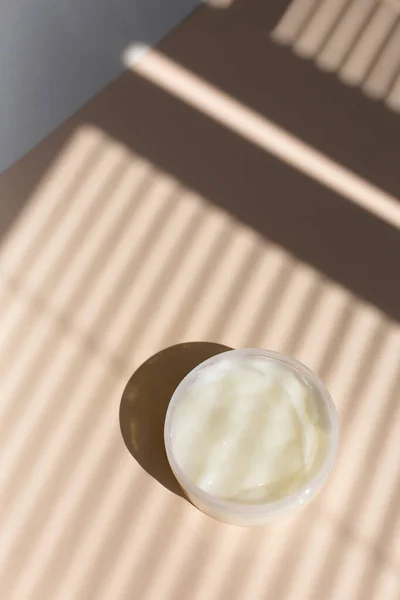 Природный эко крем для лица ручной работы в белой банке, полосатый фон тени. — стоковое фото