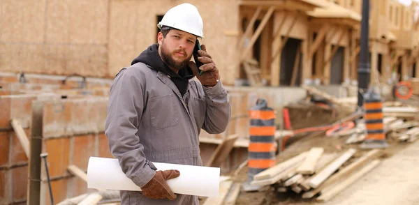 Banner do construtor falando por smartphone e segurando plano de desenho no local de construção. — Fotografia de Stock