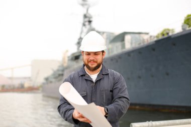 Denizcilik mühendisi planlara bakıyor ve geminin yanında duruyor..