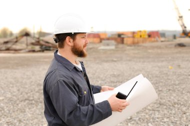 Foreman 'ın elinde VHF telsizi ve inşaat alanında kağıtlar var..