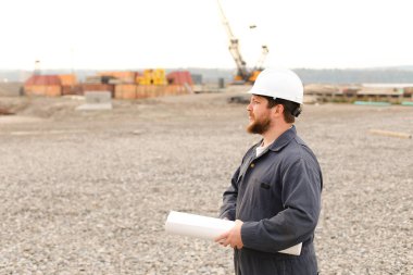 Beyaz Amerikalı ustabaşı inşaat alanının planlarını tutuyor..
