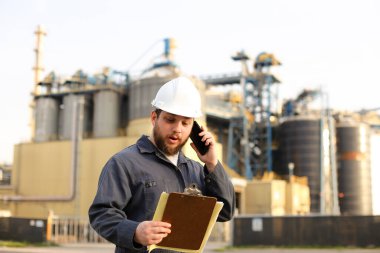 Endüstriyel direktör, VHF telsiziyle konuşuyor ve fabrikanın yakınında kağıtları tutuyor..