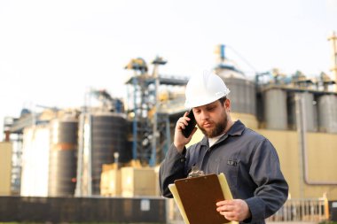 Endüstriyel Amerikan işçisi VHF telsiziyle konuşuyor ve fabrikanın önünde kağıtları tutuyor..