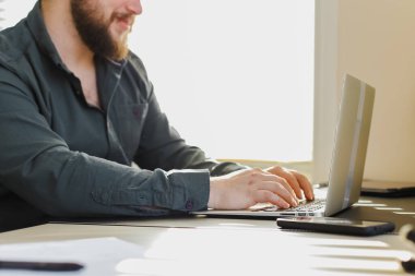 Genç web geliştiricisi ofiste dizüstü bilgisayarla çalışıyor, masada oturuyor..