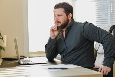 Web tasarımcısı ofis masasında oturmuş dizüstü bilgisayarla çalışıyor..