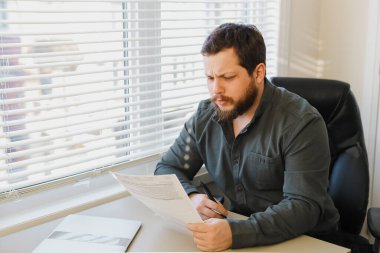 Ofiste belgelerle çalışan ekonomist, masadaki kapalı dizüstü bilgisayar..