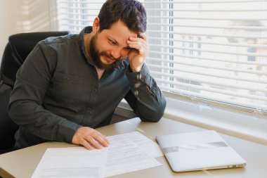 Ofisteki belgelerle çalışan başarılı bir yönetici, masadaki kapalı dizüstü bilgisayar.