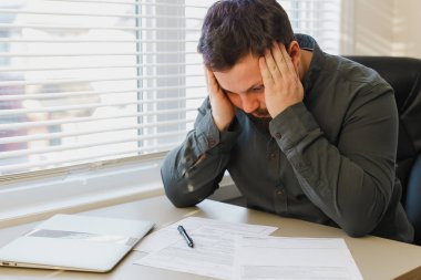 Ofisteki belgelerle çalışan beyaz bir yönetici, masadaki bilgisayarın kapalı olması üzücü..