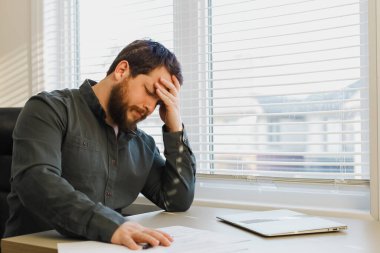 Ofiste belgelerle çalışan yorgun bir ekonomist, masada kapalı bir laptop..