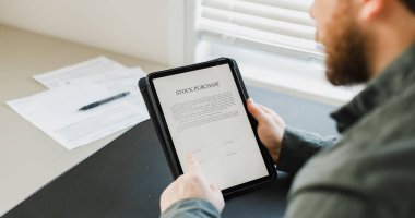 Tablet üzerinde hisse senedi satın alma sözleşmesi okuyan adam.