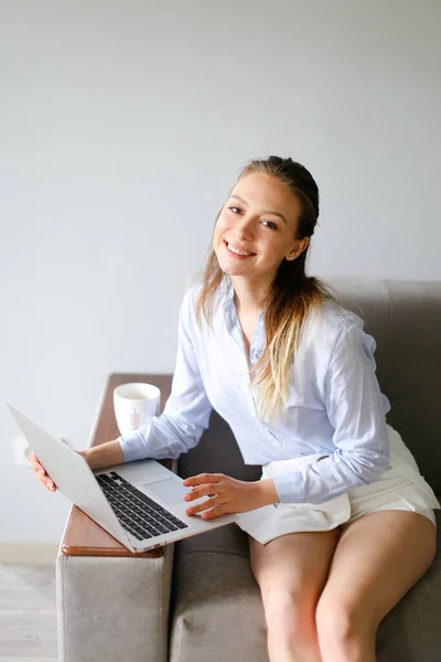 Joven mujer caucásica trabajando con el ordenador portátil en casa y sentado en el sofá. — Foto de Stock