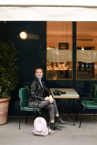年轻的微笑的女人，带着相机坐在街上的咖啡店里. — 图库照片