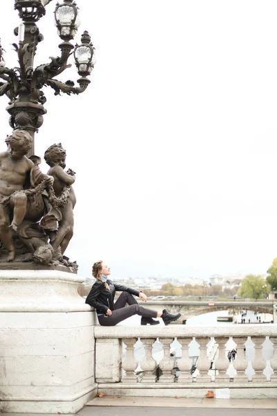 Молодая кавказка, сидящая на мосту Сена возле фонарей со скульптурой в Париже. — стоковое фото