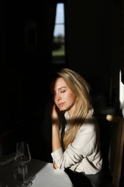 Siyah arka planda şarap kadehiyle kafede oturan genç bir kadın..