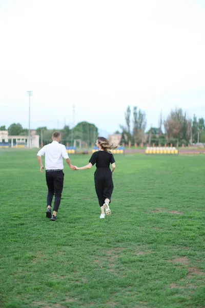 Voltar vista homem e mulher correndo no campo de futebol e de mãos dadas. — Fotografia de Stock