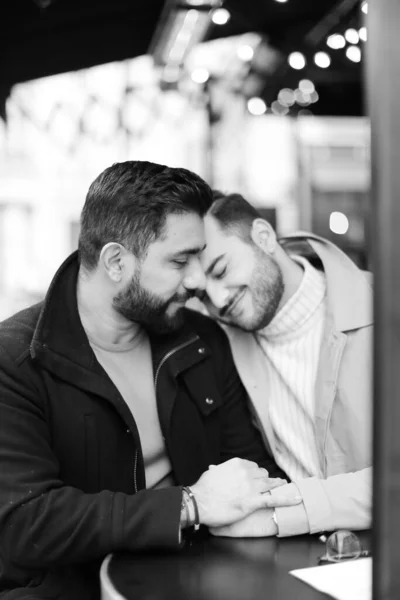 Чорно-біле фото двох кавказьких геїв, що сидять і обіймаються, тримаючись за руки . — стокове фото