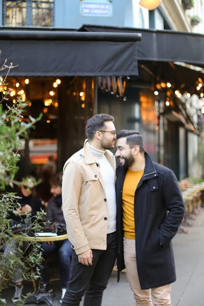 Zwei glückliche Schwule stehen in der Nähe eines Straßencafés und umarmen sich . — Stockfoto