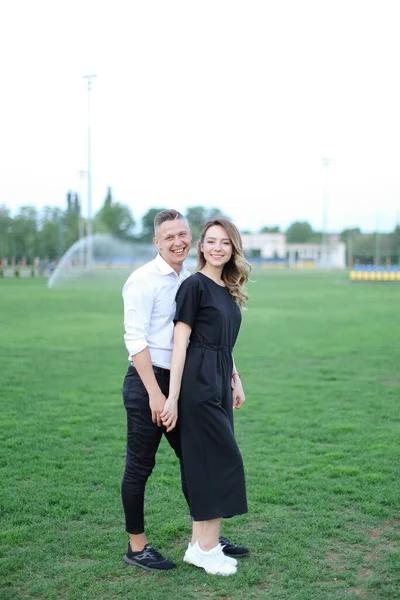 年轻的妻子牵着丈夫的手在足球场上. — 图库照片