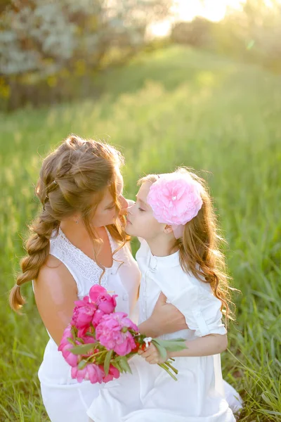 Portrait of young happy mother kissing little daughter in grass. — Stock Photo, Image