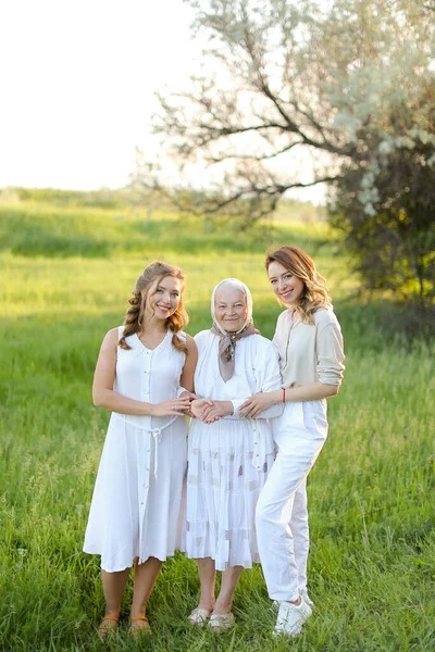 Velha avó de pé com netas adultas em vestidos brancos. — Fotografia de Stock