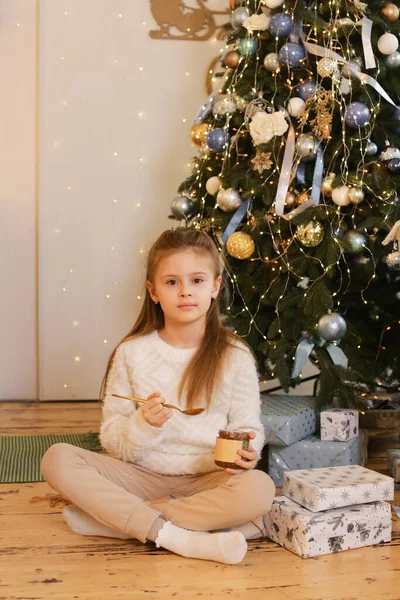 Una chica joven come mantequilla de maní en el fondo navideño de vacaciones — Foto de Stock